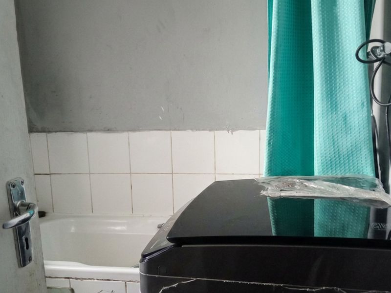 A compact bathroom featuring a bathtub with a tiled splashback, currently utilized for laundry appliance placement.