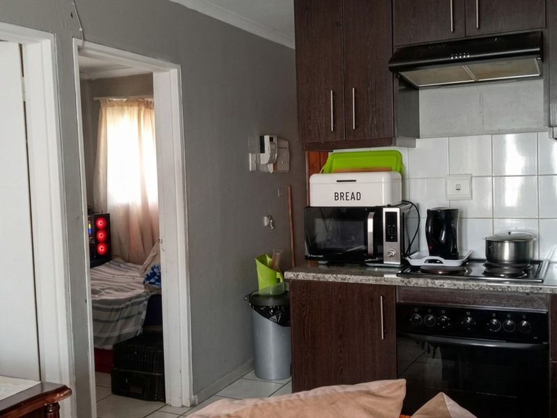 Compact kitchen featuring dark wood cabinetry, built-in oven with extractor fan, and tiled backsplash, adjacent to a bedroom doorway.