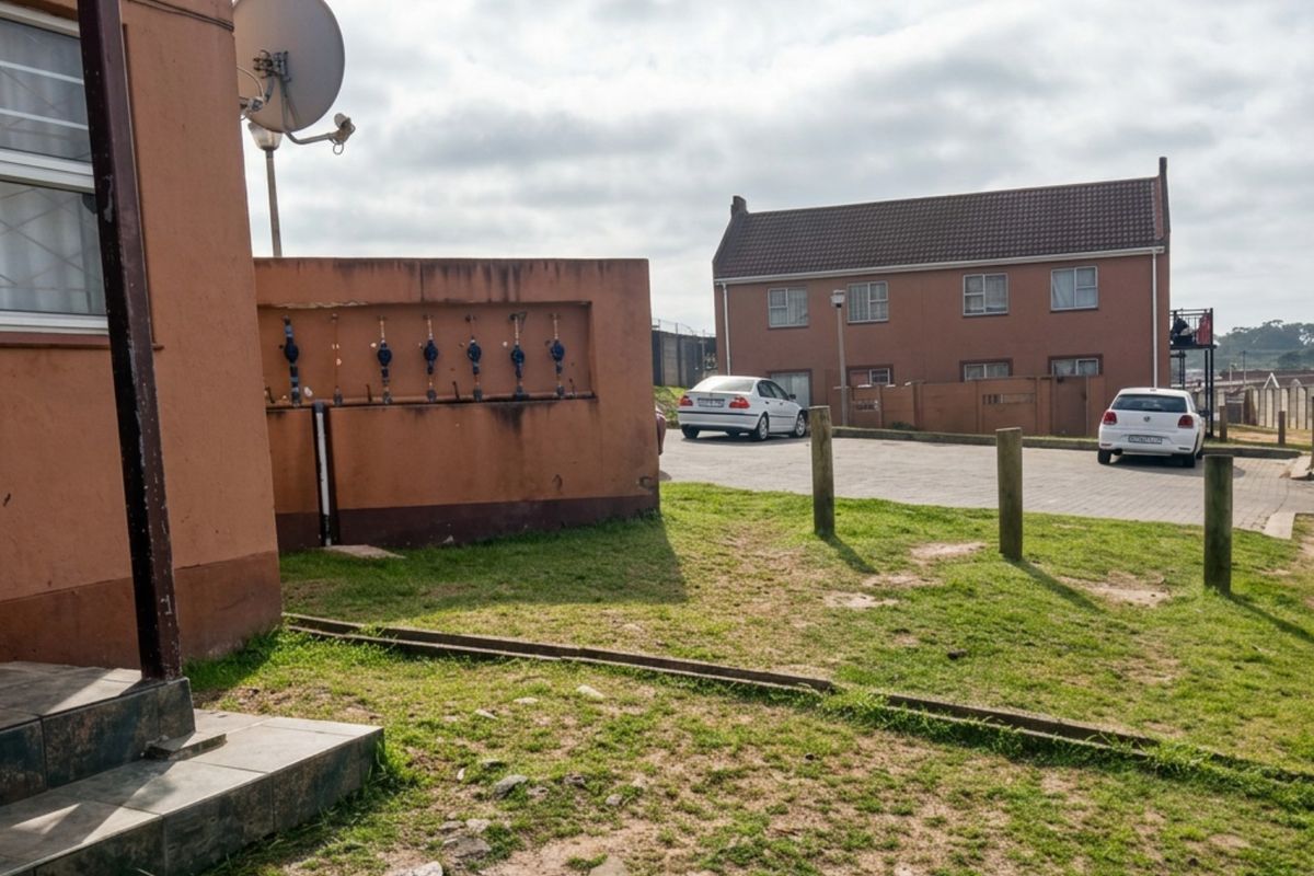 Exterior view of the apartment complex rear area featuring a paved parking lot, water meter bank, and shared outdoor space.