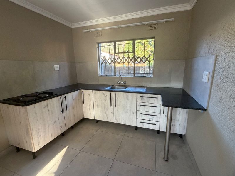 A functional kitchen featuring light wood-grain cabinetry, dark granite countertops, a built-in hob, and tiled flooring, ready for final finishing touches.