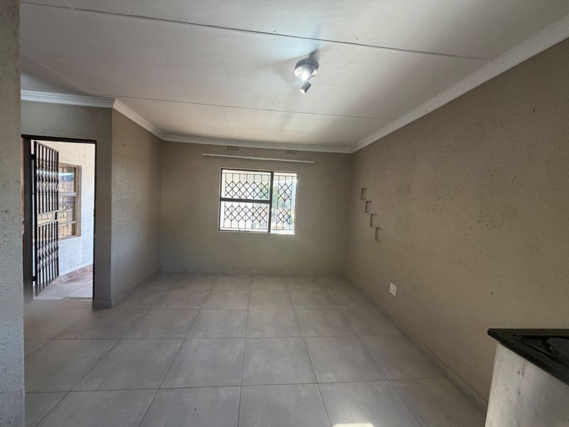 An empty open-plan living area featuring neutral tiled flooring, security bars on windows, and decorative wall niches, offering a blank canvas for personalization.