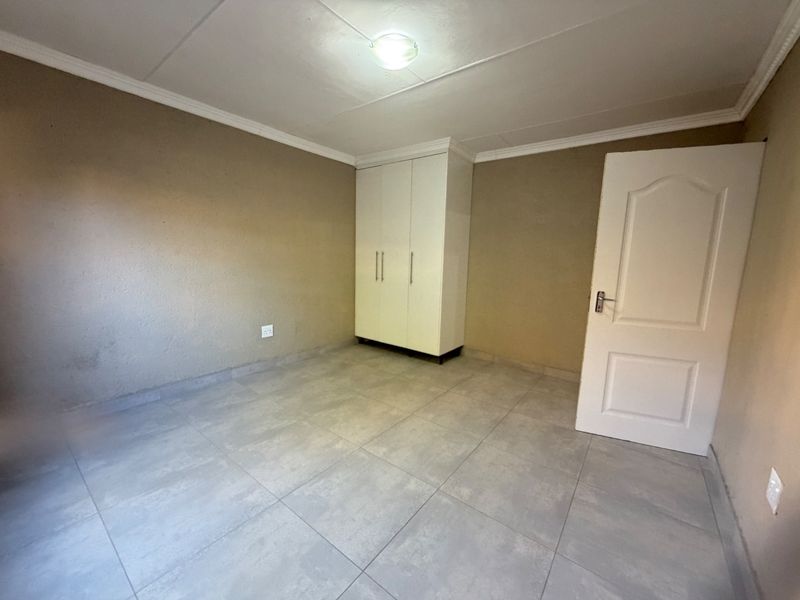 A clean, empty bedroom featuring neutral tiled flooring, a built-in white wardrobe, and a classic panel door.