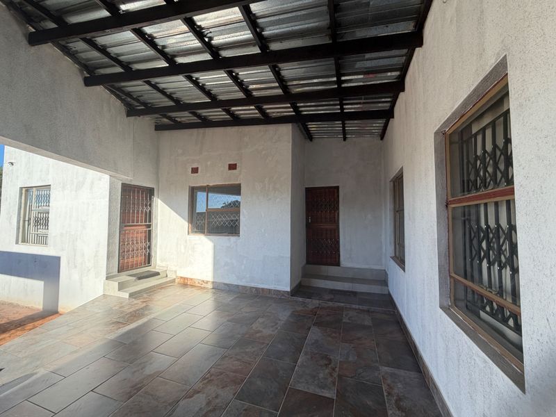 A covered outdoor patio area featuring tiled flooring, a corrugated metal roof, and secure access points with fitted security gates and window bars.