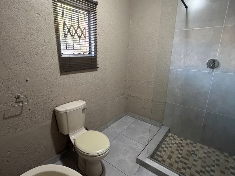 A functional bathroom featuring a walk-in shower with glass screen, tiled flooring, and standard sanitaryware.