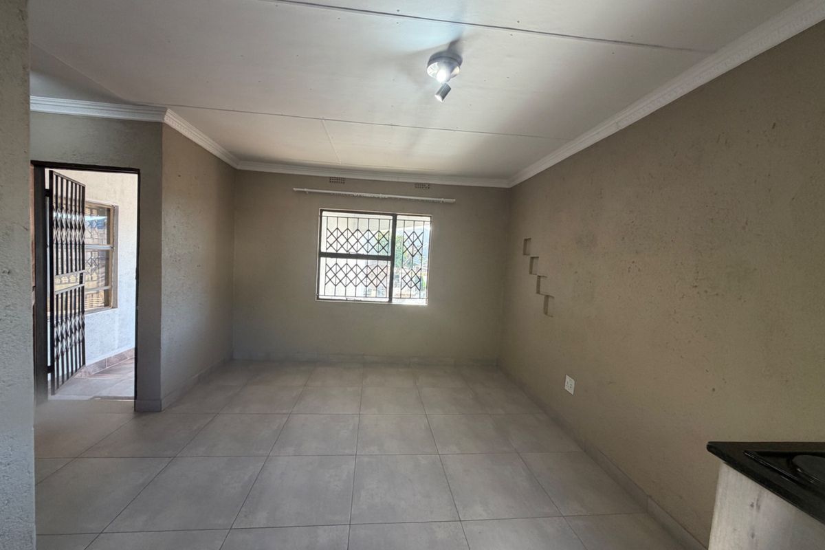 An empty open-plan living area featuring neutral tiled flooring, security bars on windows, and decorative wall niches, offering a blank canvas for personalization.