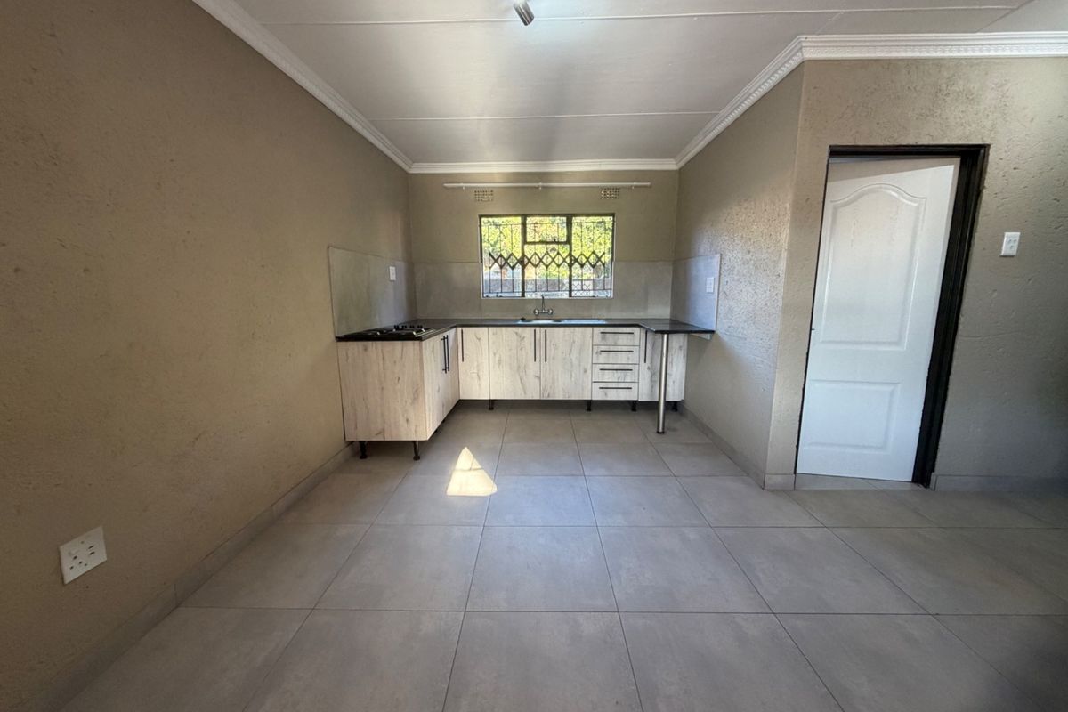 A clean, empty kitchen featuring light wood-finish cabinetry, dark countertops, a built-in hob, and neutral tiled flooring.