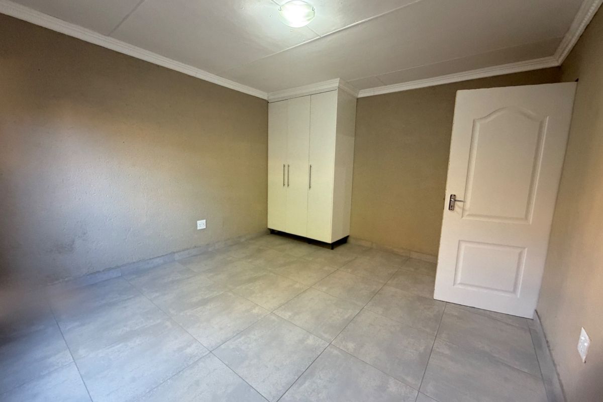 A clean, empty bedroom featuring neutral tiled flooring, a built-in white wardrobe, and a classic panel door.