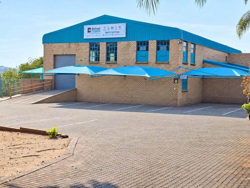 Commercial warehouse building featuring a brick facade, roller shutter door, access ramp, and paved parking area with shade cloth carports.
