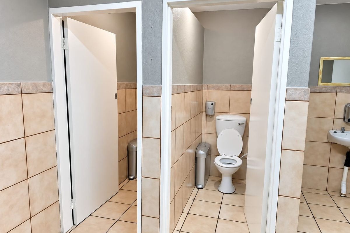 Commercial bathroom facility featuring tiled walls and floors, individual toilet cubicles, and a pedestal basin.