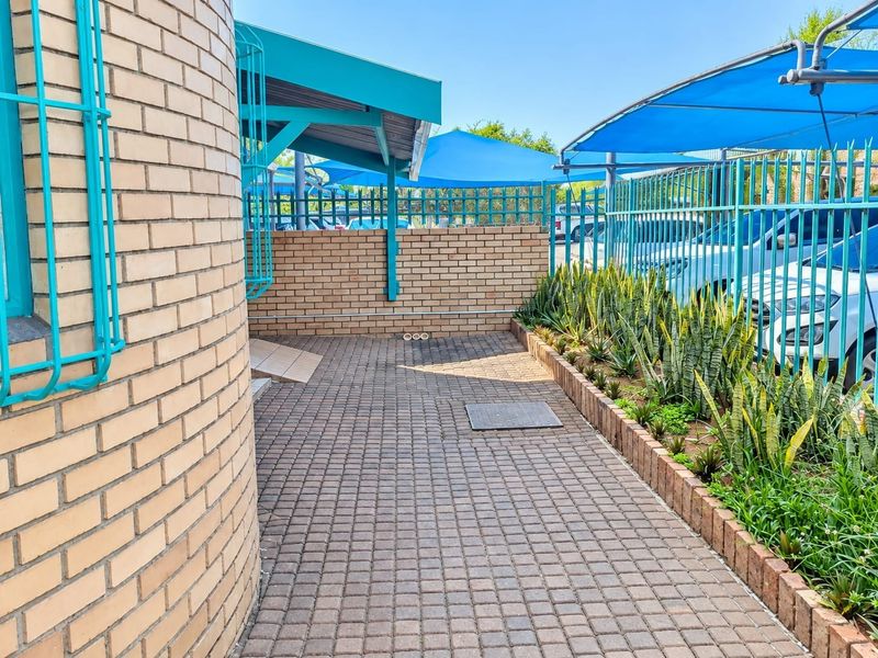 A paved outdoor area featuring a brick boundary wall, metal security fencing, and overhead shade sails, providing a secure and functional exterior space.
