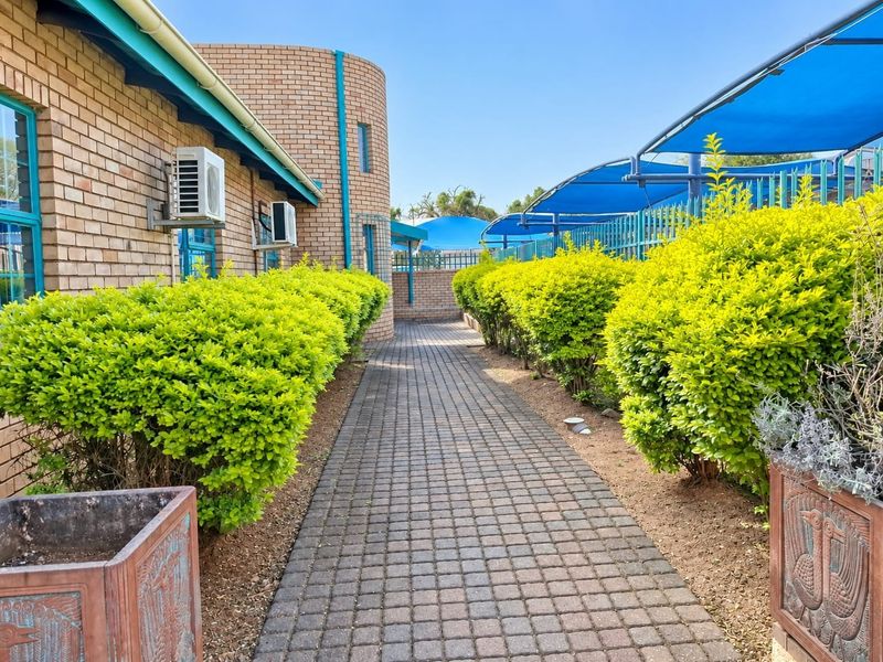 A well-maintained exterior walkway featuring brick building facades, paved pathways, established hedging, and overhead shade structures for outdoor comfort.