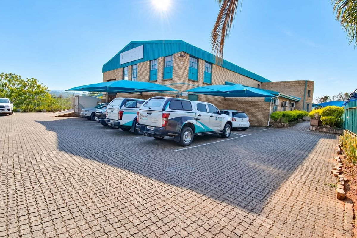 Commercial property exterior featuring a face brick facade, metal roofing, and a paved parking area with shade cloth carports.