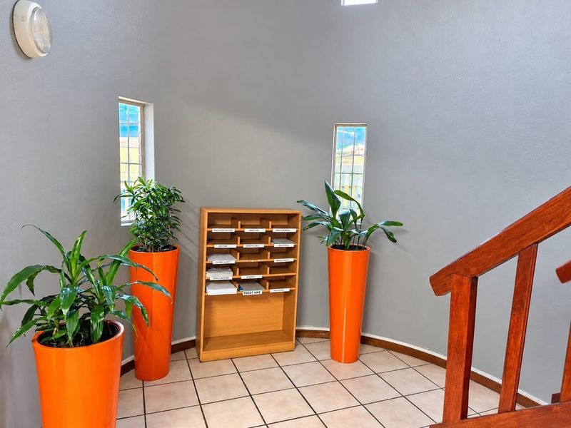 A bright hallway area featuring tiled flooring, vertical windows, and a wooden staircase railing, providing a clean and functional transition space.