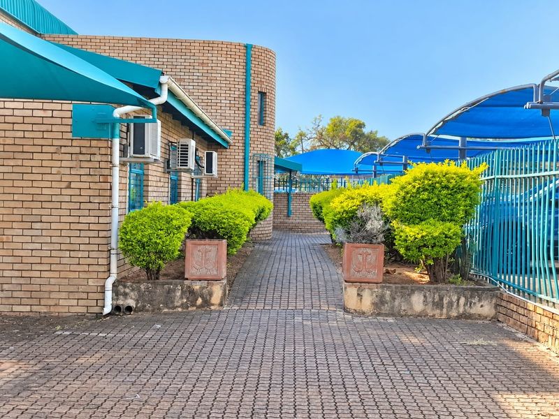 Exterior view of a commercial property featuring a paved walkway, brick facade, and shaded parking areas with metal security fencing.
