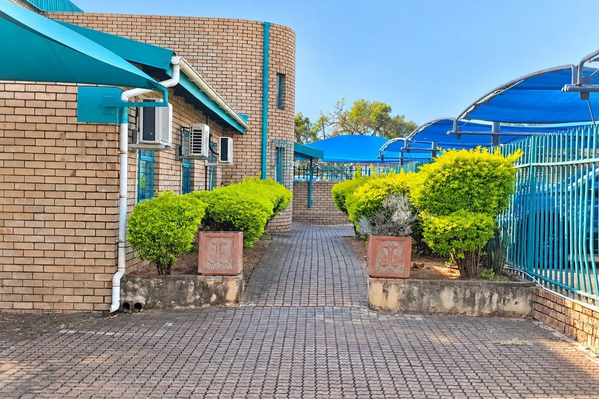 Exterior view of a commercial property featuring a paved walkway, brick facade, and shaded parking areas with metal security fencing.