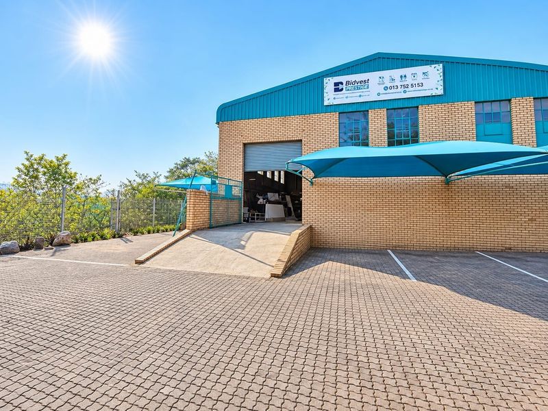 Commercial property exterior featuring a face brick facade, roller shutter door with concrete loading ramp, paved parking area, and installed shade sail structures.