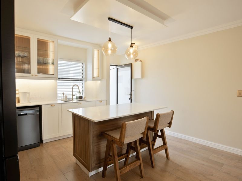 Modern kitchen featuring white cabinetry, quartz countertops, a central island with seating, integrated dishwasher, and stylish pendant lighting.