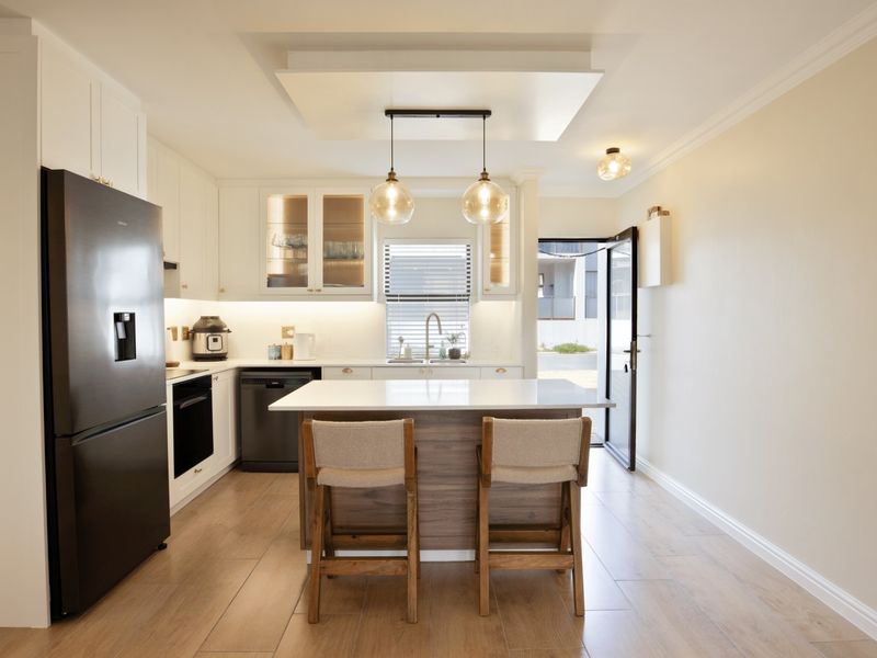 Modern kitchen featuring white cabinetry, quartz countertops, a central island with seating, integrated appliances, and stylish pendant lighting, opening to an outdoor area.
