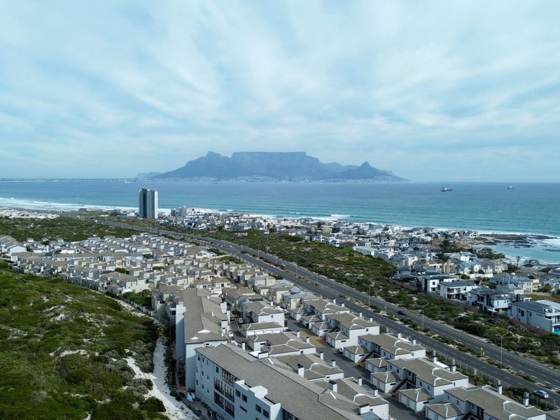 Aerial view of a coastal residential estate featuring panoramic views of the ocean and Table Mountain in the distance.