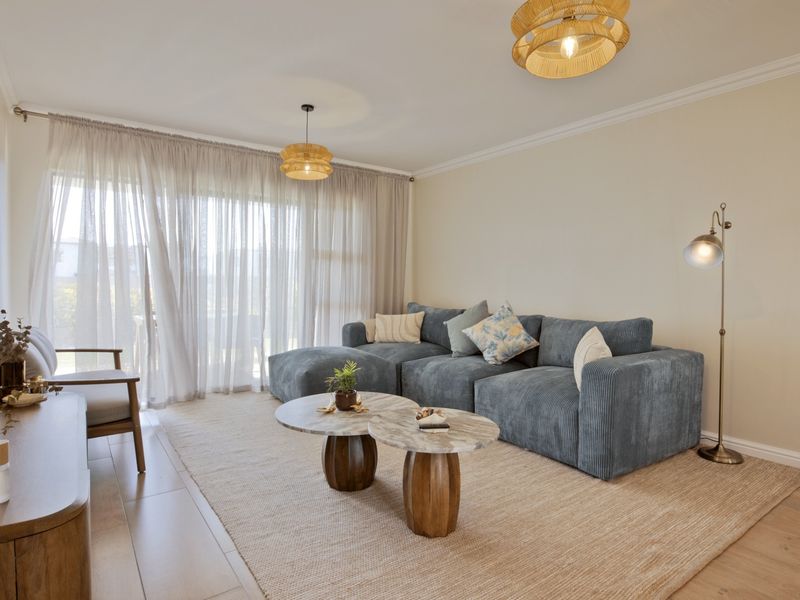 A bright and inviting living room featuring neutral walls, crown molding, laminate flooring, and large sliding glass doors that provide ample natural light.