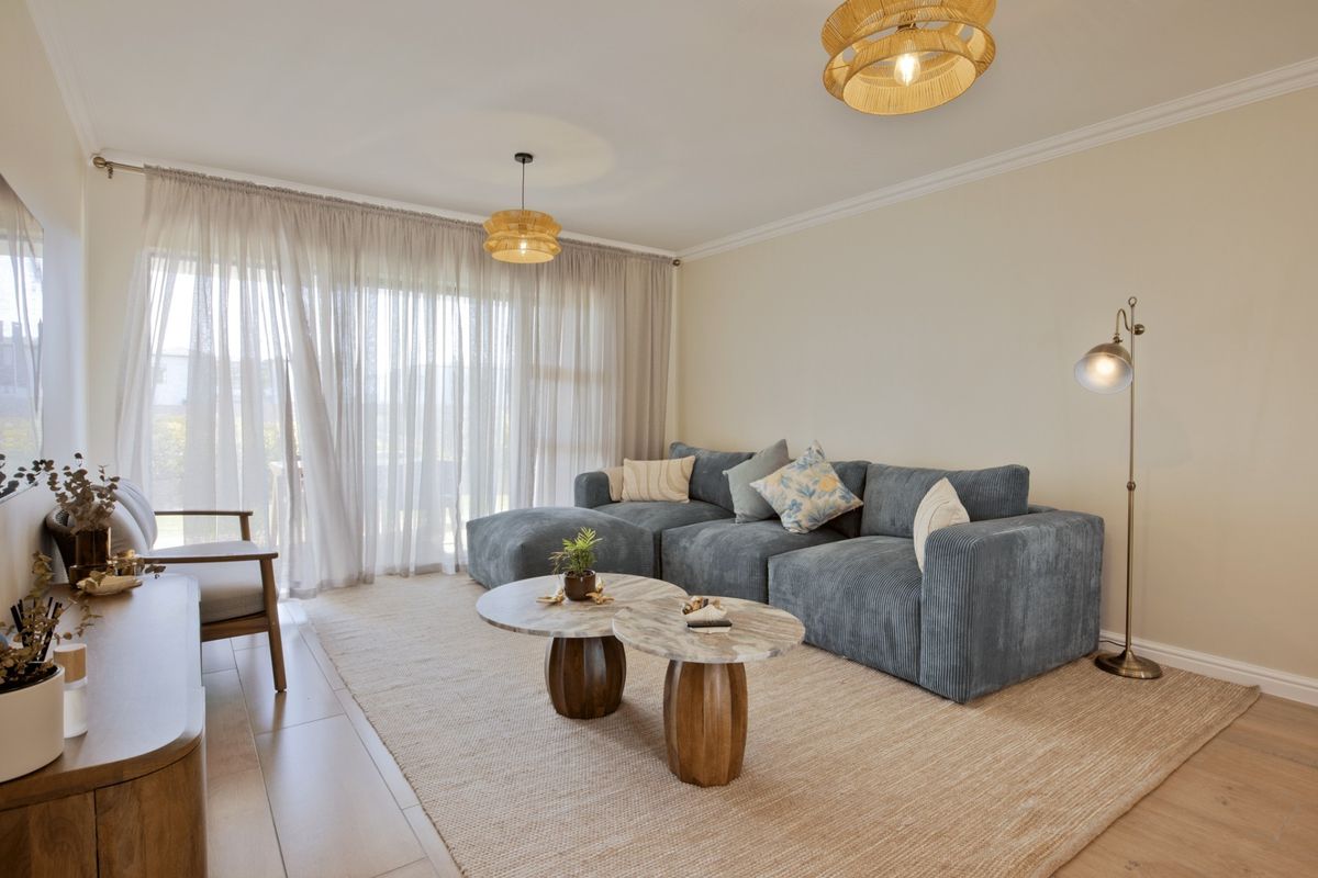 A bright and inviting living room featuring neutral walls, crown molding, laminate flooring, and large sliding glass doors that provide ample natural light.