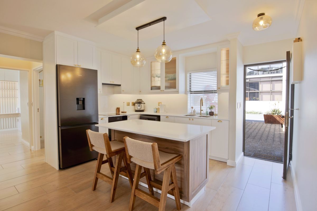 Modern kitchen featuring white cabinetry, quartz countertops, a central island with seating, and high-quality finishes, with direct access to an outdoor area.