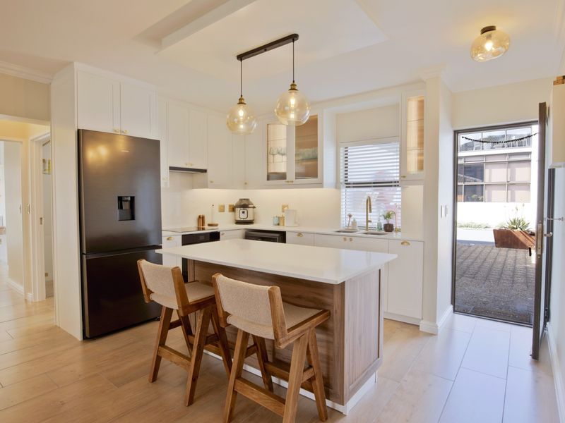 Modern kitchen featuring white cabinetry, quartz countertops, a central island with seating, and high-quality finishes, with direct access to an outdoor area.
