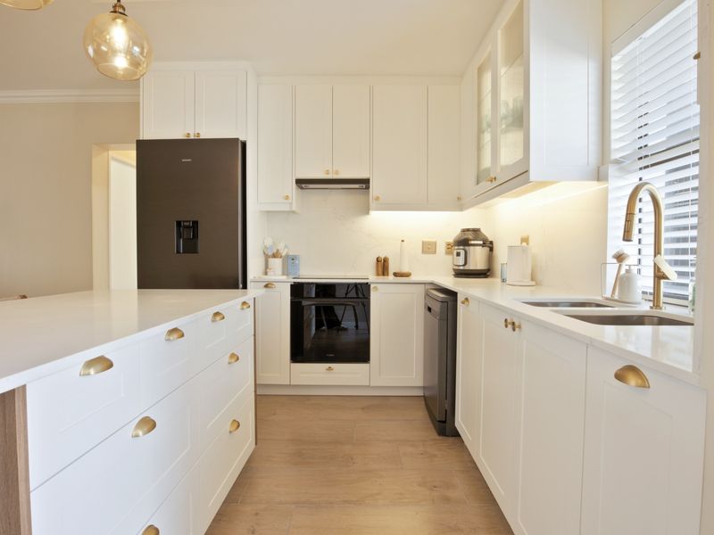 Modern kitchen featuring white cabinetry, stone countertops, brass hardware, integrated appliances, and a functional kitchen island with ample storage.
