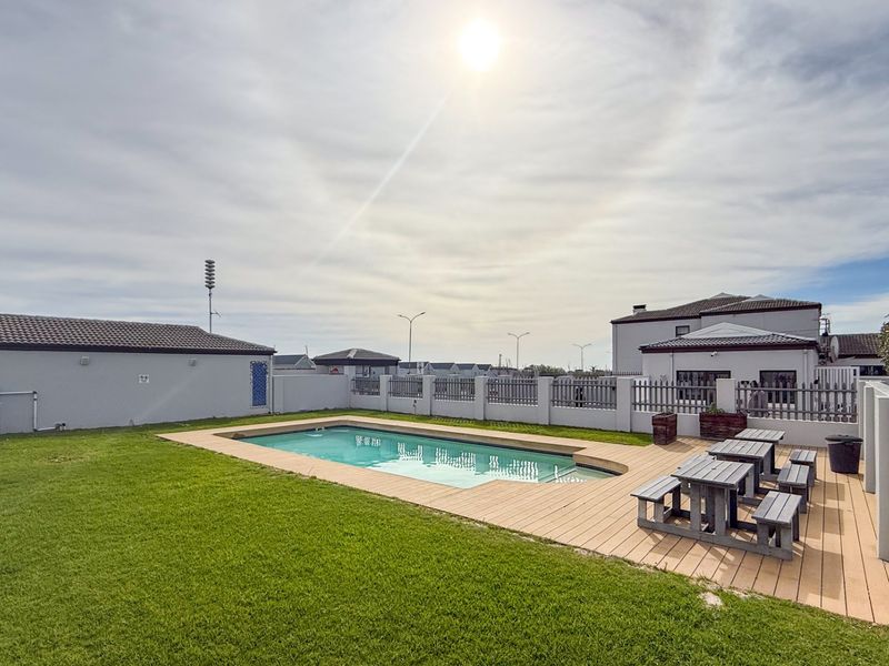 Outdoor communal pool area featuring a swimming pool, timber decking, and surrounding lawn within a secure complex.