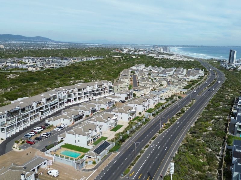 Aerial view of a coastal residential apartment complex featuring paved parking, a swimming pool, and proximity to the beach and main road.