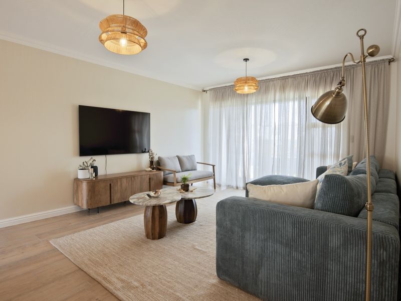 A bright and modern living room featuring light wood-look laminate flooring, neutral walls, and a large sliding glass door providing ample natural light.