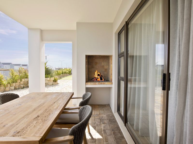A covered patio featuring a built-in fireplace, brick flooring, and sliding glass doors, offering a seamless transition to the outdoor garden area.