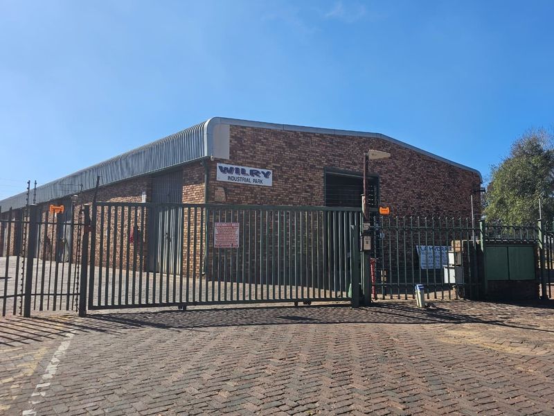 Front view of Wilry Industrial Park featuring a brick facade, secure steel gate entrance, electric fencing, and paved driveway access.