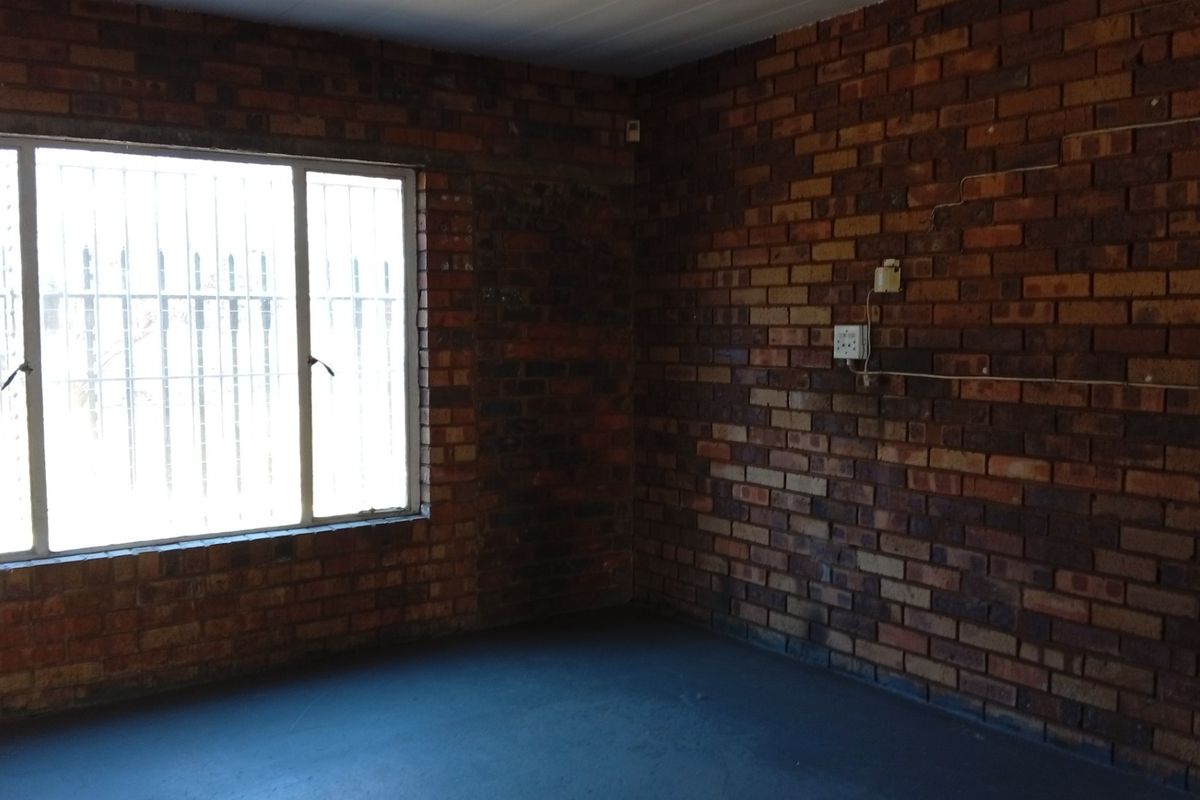 An empty room featuring exposed brick walls, security bars on the window, and painted concrete flooring, suitable for various commercial uses.