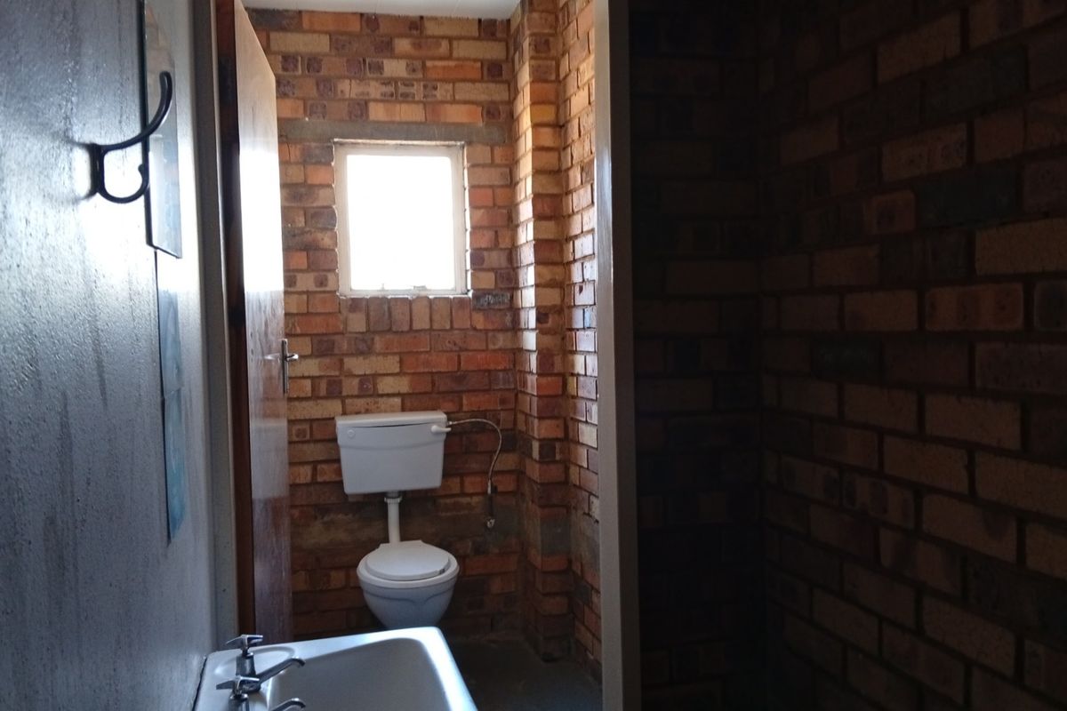 A functional bathroom featuring exposed brick walls, a standard toilet, and a wall-mounted washbasin with basic plumbing fixtures.