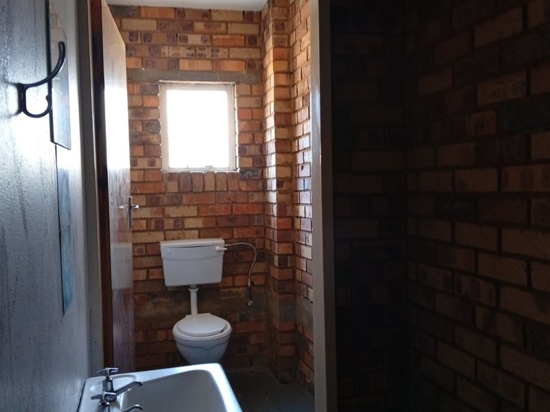 A functional bathroom featuring exposed brick walls, a standard toilet, and a wall-mounted washbasin with basic plumbing fixtures.