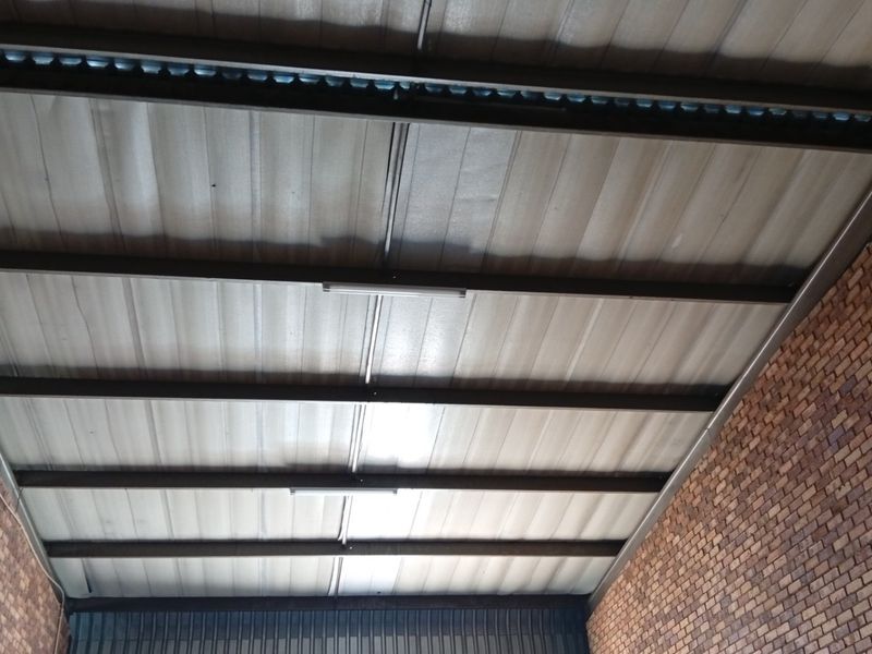 A view of a commercial garage interior featuring exposed steel roof beams, corrugated metal ceiling panels, and exposed brick walls.