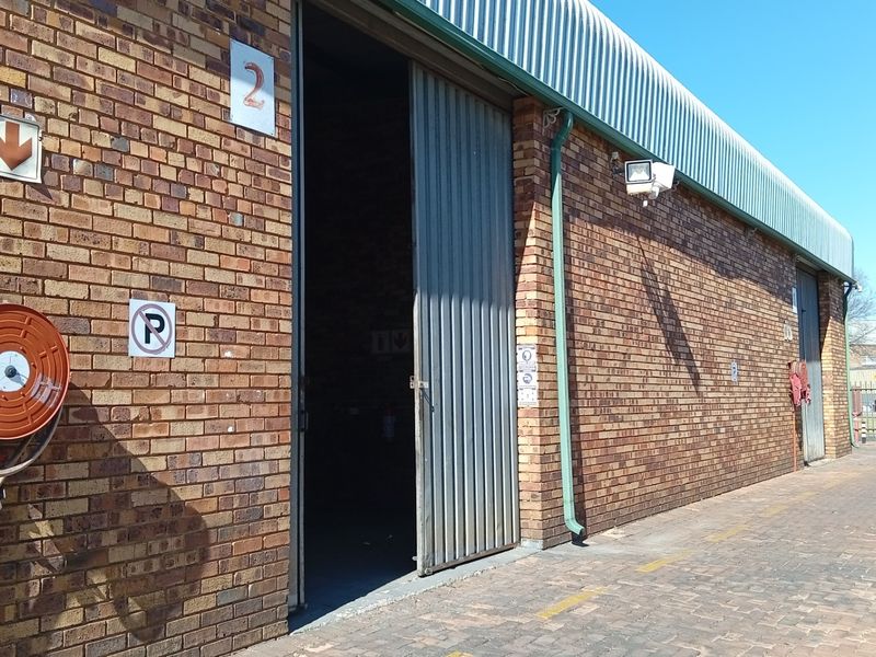 Exterior view of a commercial industrial unit featuring face brick walls, a large sliding metal door, and a fire hose reel installation.