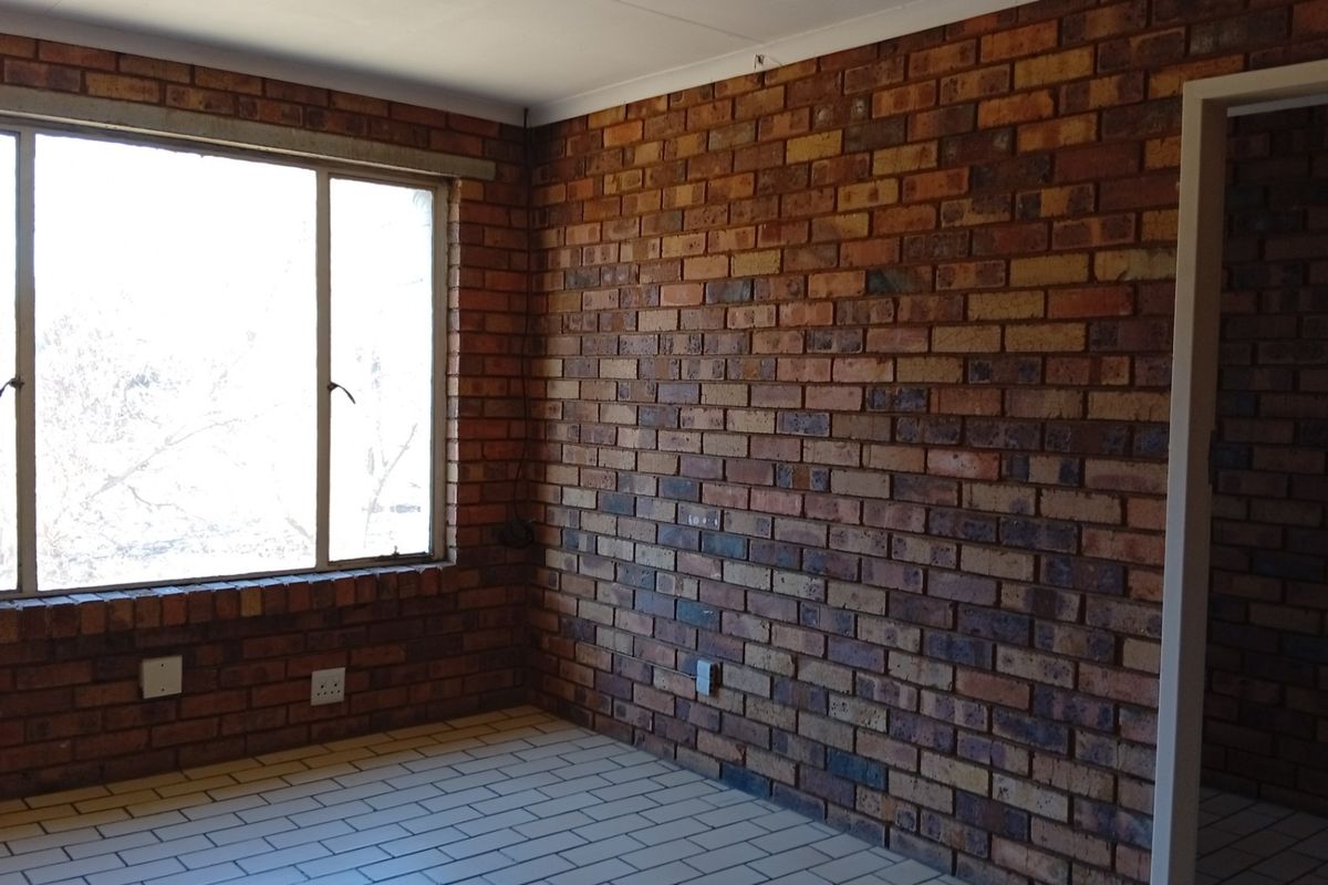 An empty bedroom featuring exposed brick walls, tiled flooring, and a large window providing natural light.