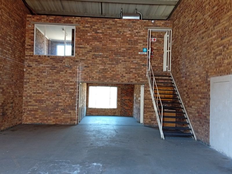 Spacious industrial utility area featuring exposed brick walls, concrete flooring, and a metal staircase leading to a mezzanine level.