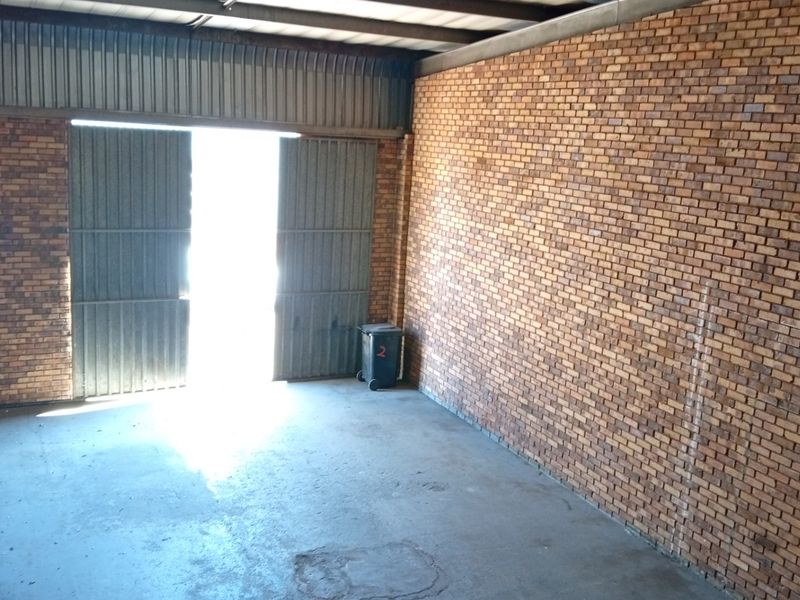A spacious, empty commercial garage featuring exposed brick walls, concrete flooring, and a large metal roller door entrance.