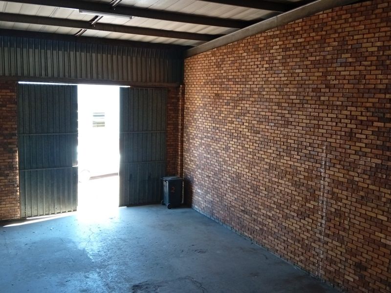 A spacious, empty commercial garage featuring exposed brick walls, concrete flooring, and high-clearance metal doors, suitable for storage or workshop use.