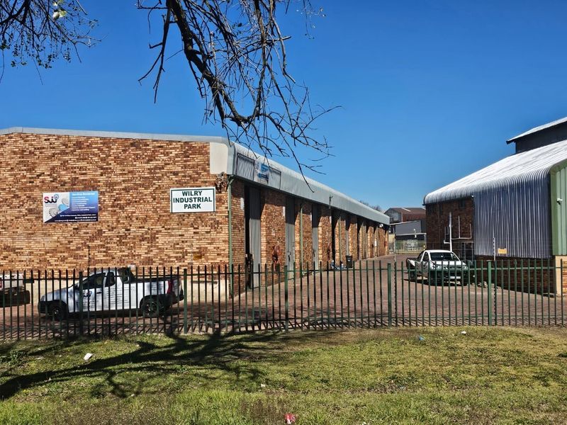 Exterior view of Wilry Industrial Park featuring brick warehouse units with metal roller shutter doors, paved driveway, and secure perimeter fencing.
