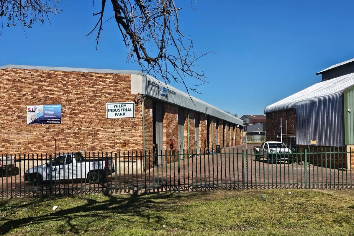 Exterior view of Wilry Industrial Park featuring brick warehouse units with metal roller shutter doors, paved driveway, and secure perimeter fencing.