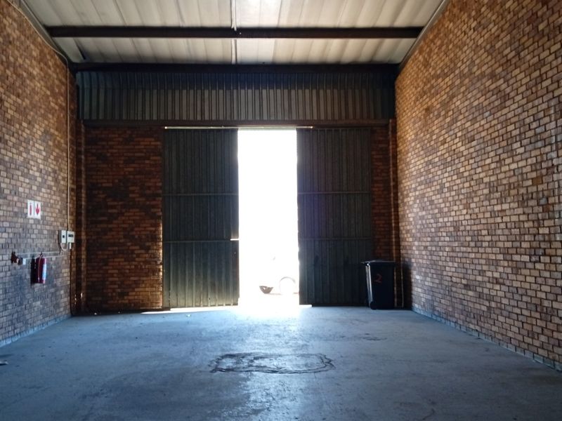 Spacious industrial garage or warehouse unit featuring exposed brick walls, concrete flooring, and large sliding metal doors for vehicle or equipment access.