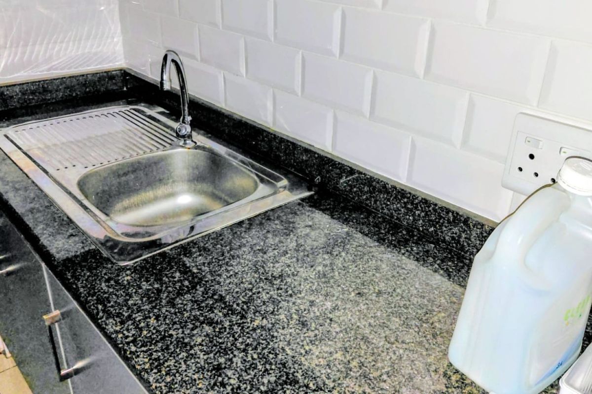 A clean kitchen area featuring a dark granite countertop, stainless steel sink, and white subway tile backsplash.