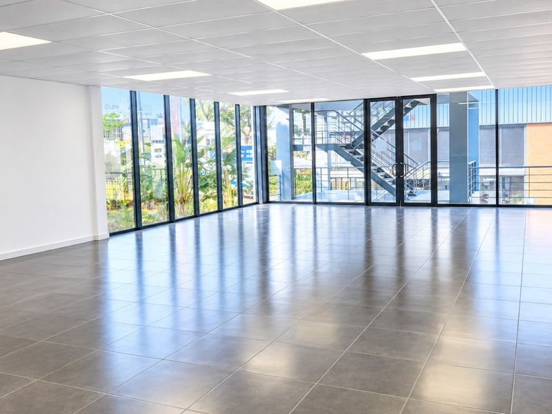 A bright, modern open-plan commercial office space featuring large floor-to-ceiling windows, tiled flooring, and a clean, professional suspended ceiling.