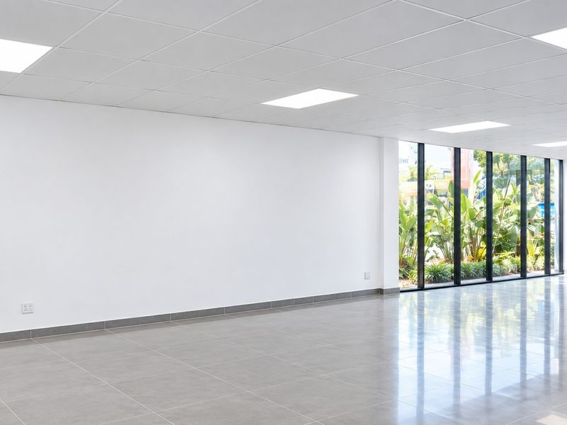 A bright, modern, and vacant commercial office space featuring polished tiled floors, a suspended ceiling with recessed lighting, and large floor-to-ceiling windows.