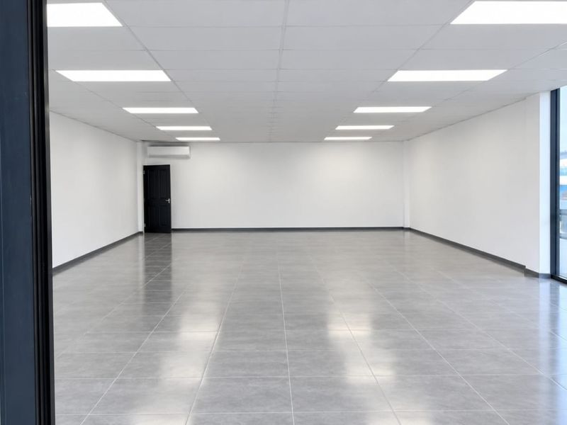 A bright, modern, and vacant commercial office space featuring tiled flooring, recessed lighting, and large windows providing ample natural light.