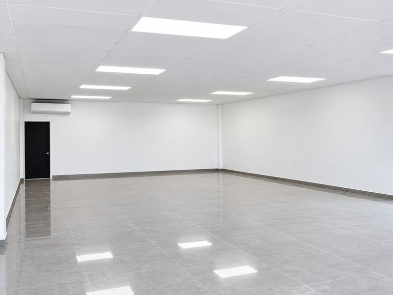 A bright, modern, and spacious open-plan office area featuring polished tiled floors, a suspended ceiling with recessed lighting, and split-system air conditioning.
